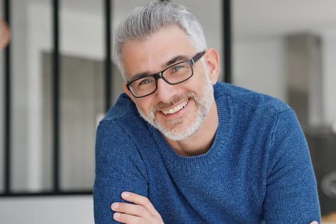 Restorative Dentistry Solutions | Repair Broken, Lost Teeth | We Care Dental Patient with glasses and grey beard smiling proudly after restorative dentistry: repaired broken teeth and renewed confidence.