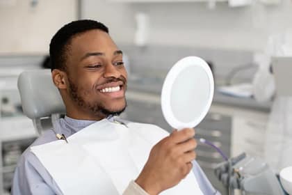 Beaming Smile After Dental Implants in Dublin, CA | We Care Dental - Dr. Chona Lardizabal Smiling man examining his new dental implants in a mirror at We Care Dental in Dublin, CA with Dr. Chona Lardizabal