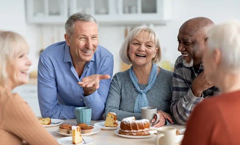 Seniors laughing together outdoors, holding coffee cups, with bright smiles highlighting the confidence and joy of healthy aging through quality dental care.
