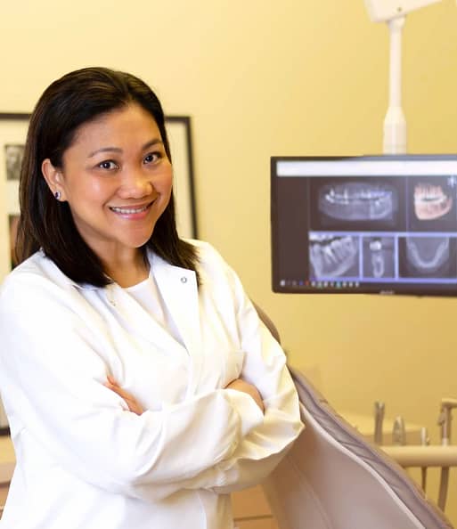 Dr. Chona Lardizabal | Compassionate Dublin Dentist | We Care Dental Dr. Chona Lardizabal, Dublin CA Dentist, smiling warmly in a white coat at We Care Dental’s modern office, holding a model of teeth to demonstrate patient education.