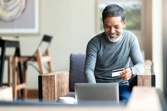 Check Insurance & Book Online at We Care Dental - From Home A man at home uses a laptop to schedule an appointment on the We Care Dental website, holding his insurance card ready to check coverage.
